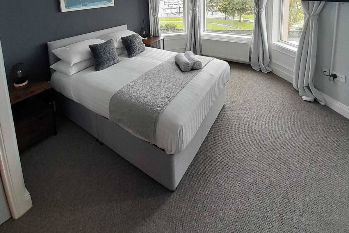 A bedroom with a large bed, a world map on the wall, and a view of the outdoors through the windows.