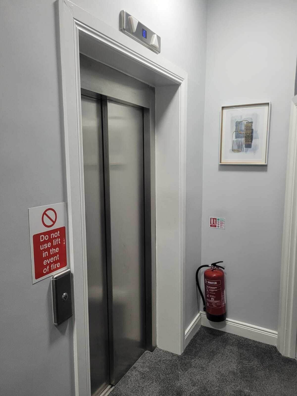 An elevator with a fire safety sign, a fire extinguisher, and a framed picture on the wall.