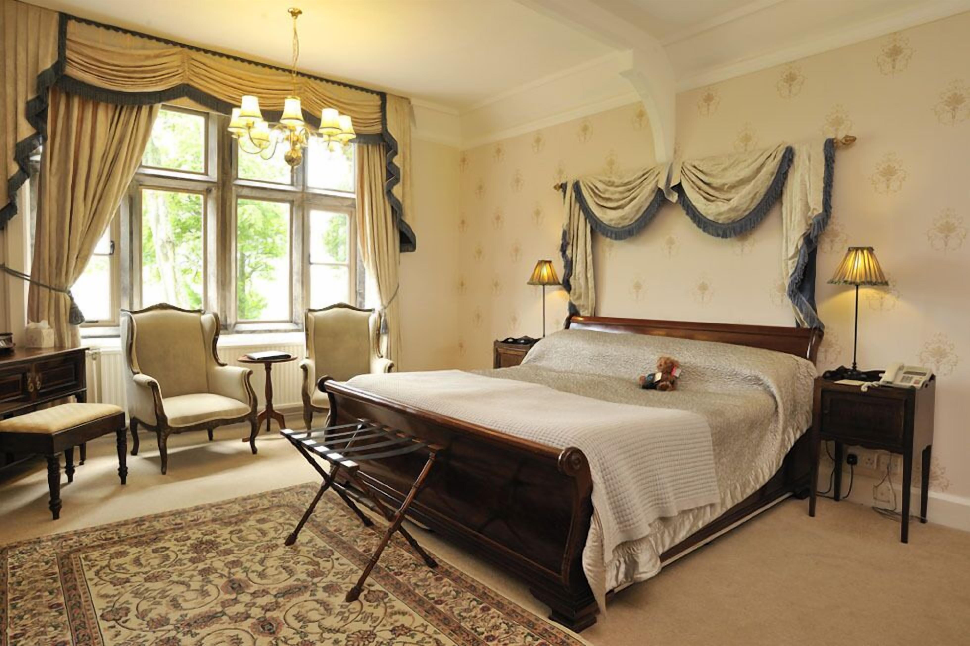 A classic bedroom with a large bed, two bedside tables, a chair, a desk, and a lamp.