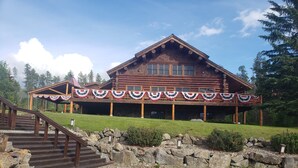 A wooden lodge with a covered porch decorated with red, white, and blue bunting, a stone staircase, and a well-maintained lawn. - Rustic 1 bedroom, 1 bath, 2 minutes from the West Glacier Park (West Glacier)