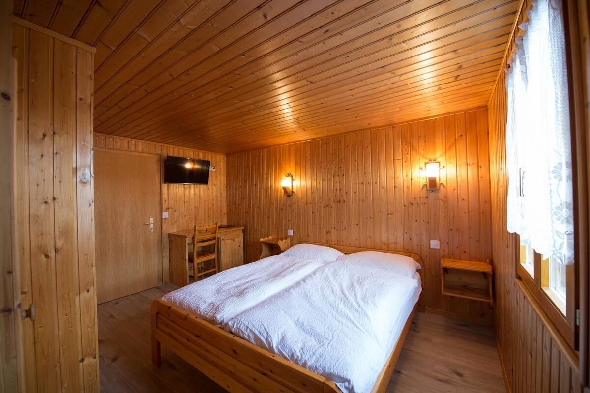 A wooden-paneled room with a bed, a desk, and two wall-mounted lights.