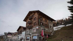 Un hotel in tipico stile chalet con ristorante al piano terra, situato ai piedi di una collina con una strada che si inerpica verso l'alto.