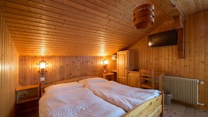 Una camera da letto in un rifugio di legno con un letto grande, due luci a parete, un televisore e un termosifone.