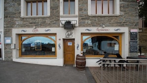 Un edificio in pietra con un caffè e un ristorante al piano terra, caratterizzato da ampie finestre ad arco e una porta in legno.