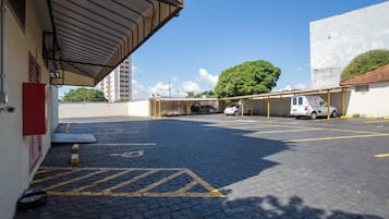 Zona d'aparcament amb una part coberta i un edifici amb una porta vermella.