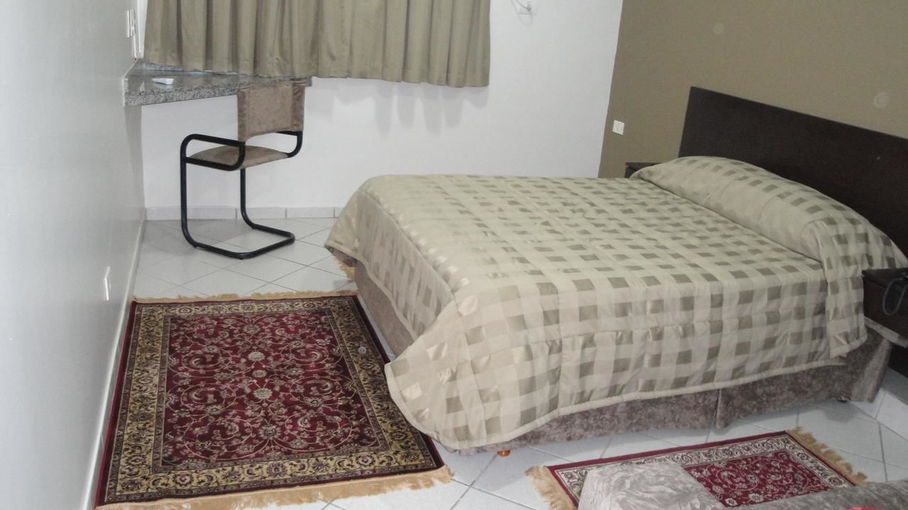 Una habitación pequeña con cama, una silla y una ventana con cortinas.