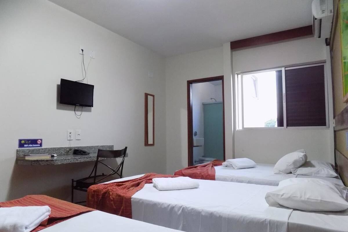 A hotel room with two beds, a desk, a chair, a TV, and a window.