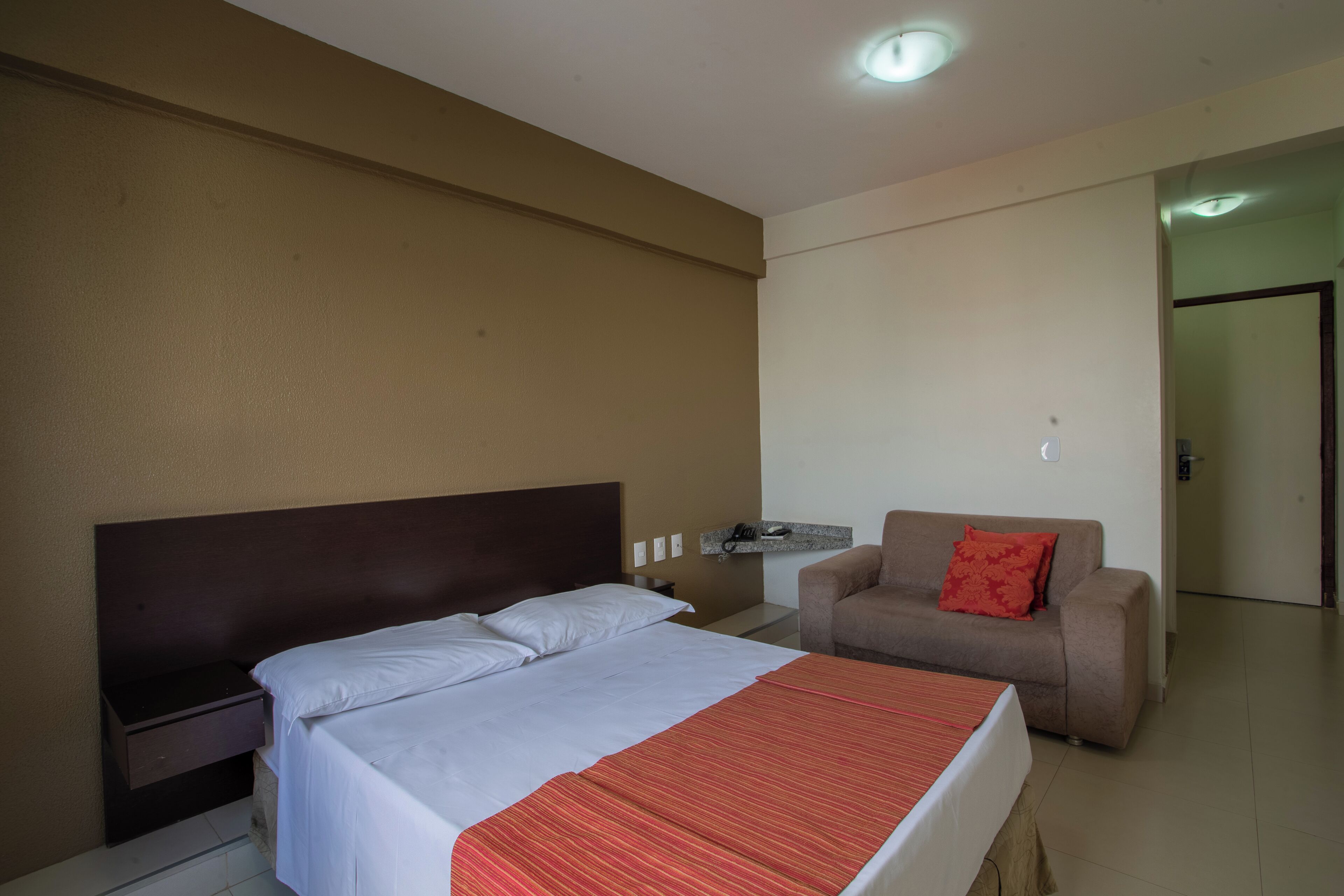 Quarto de hotel com cama, mesa de cabeceira, cadeira e pequena mesa.