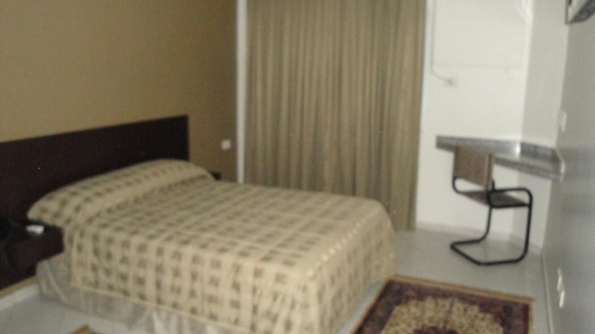 Une chambre d’hôtel avec un lit, une table de chevet, une chaise, un rideau et une petite table.