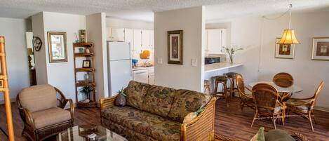 A living room with a sofa, armchairs, a coffee table, and a dining area with wicker furniture.