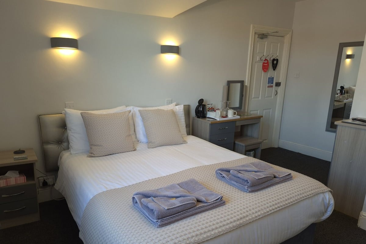 A hotel room with a bed, bedside tables, a desk, a mirror, and a wardrobe.