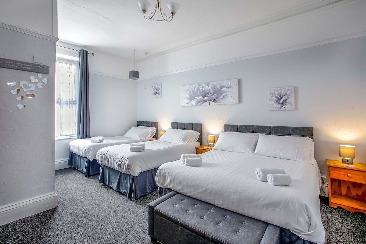 A hotel room with two beds, a bench, and a nightstand with a lamp.