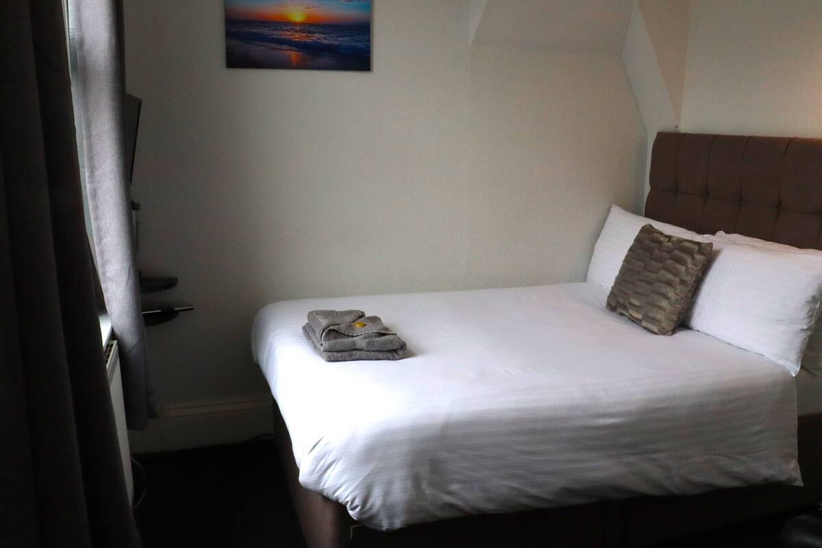 A neatly made bed with a folded towel, a headboard, and a painting on the wall.