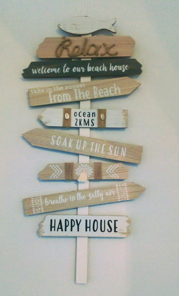 A wall-mounted sign with various phrases like "Relax," "Welcome to our beach house," and "Happy House," suggesting a welcoming and relaxing atmosphere.