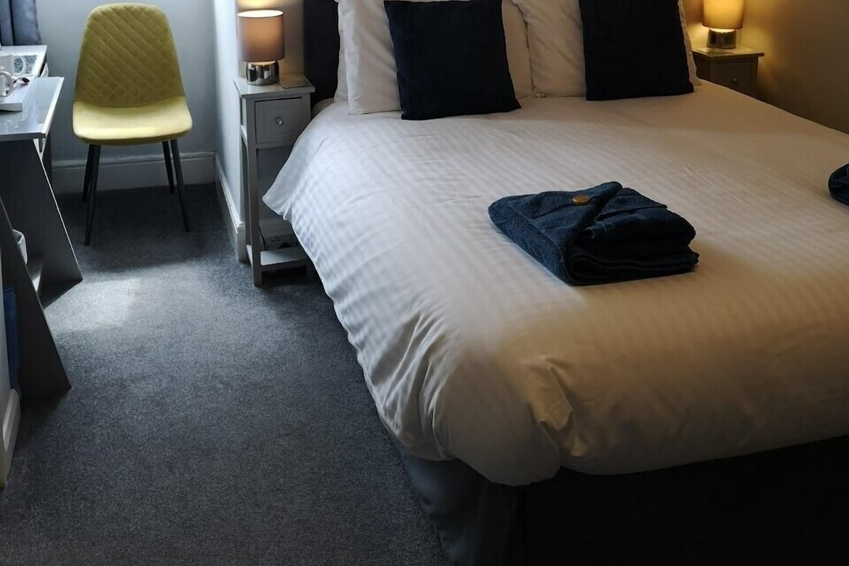 A hotel room with a bed, a chair, a desk, and a window.