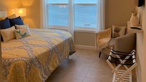 Ein Schlafzimmer mit Bett, einem Sessel, einem kleinen Tisch, einem Deckenventilator und einem Fenster mit Meerblick.
