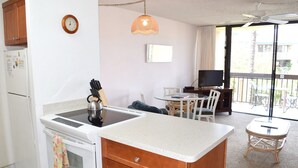 Cocina compacta con estufa, lavamanos y armarios de madera. Cuenta con una zona de comedor con mesa y sillas, además de un balcón con televisor.