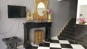 A black and white checkered floor, a black console table with a gold mirror, a gold cabinet, and a staircase with black steps. - Hotler Boutique Apartment (Pattaya)