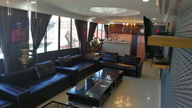 A modern living room with a sofa set, a glass coffee table, and a kitchen area in the background. - Hotler Boutique Apartment (Pattaya)