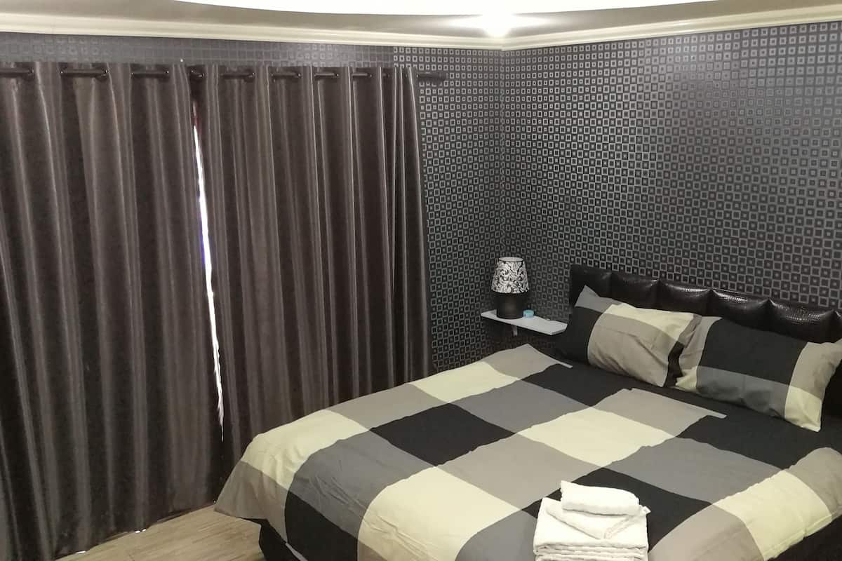 A hotel room with a bed, curtains, a patterned wall, a nightstand, and a lamp.