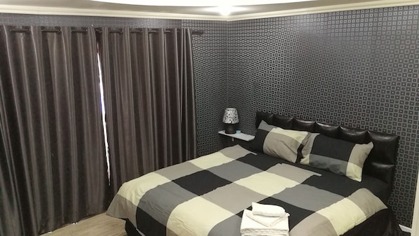 A hotel room with a bed, a nightstand, a lamp, and a curtain.