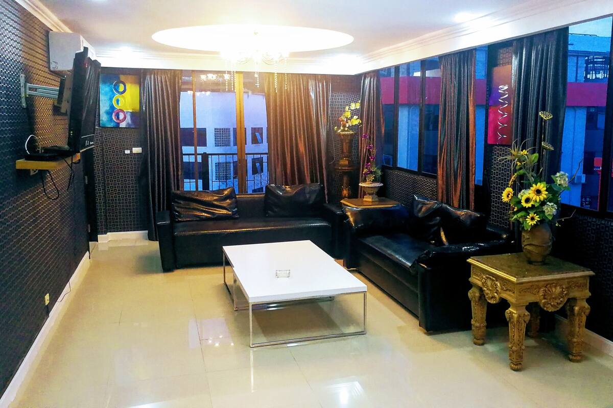 A modern living room with a black leather sofa, a white coffee table, and a decorative vase with flowers.