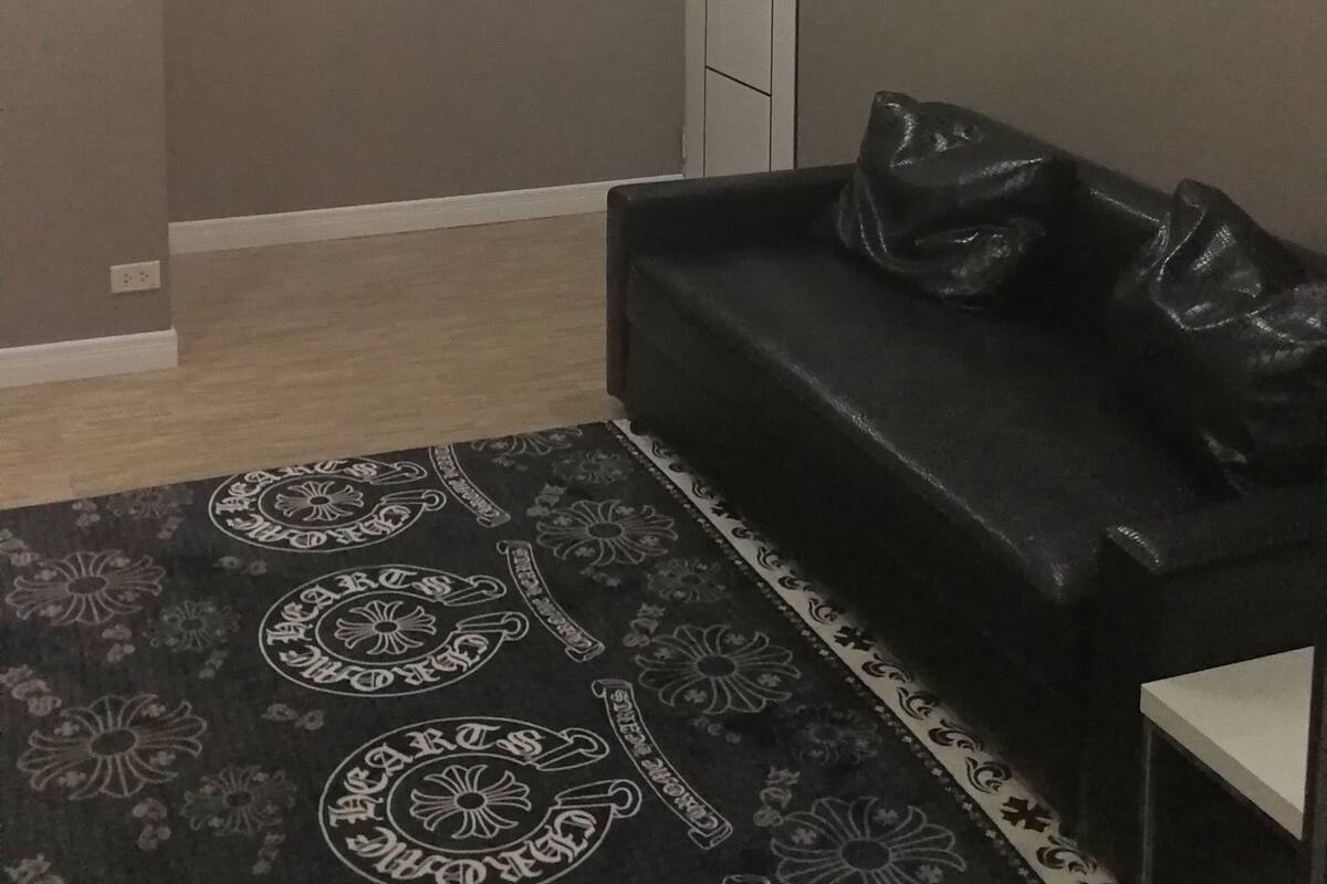A room with a chandelier, a black leather sofa, a patterned rug, and a door.