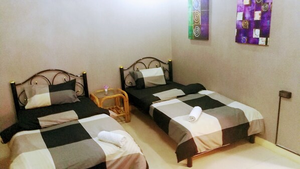 Una habitación con dos camas, cada una con colcha y almohadas a cuadros. Entre las camas, una mesita de madera con un jarrón de flores.