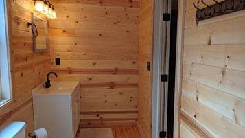 A wooden cabin bathroom with a sink, mirror, and towel dispenser.