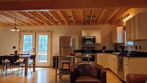 A spacious kitchen with wooden beams, a dining area with a table and chairs, and a cozy seating area with a leather couch. - Peacefull, private Cabin! 140 acres,mile of river trails! 10 minutes to Rt.151! (Faber)