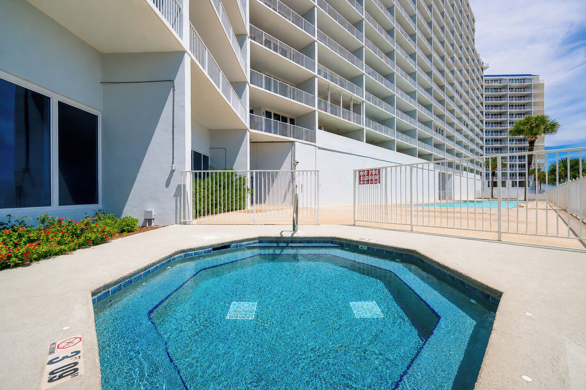 A modern hotel with a swimming pool, multiple balconies, and a clear sky.