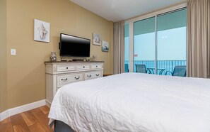 Quarto de hotel com cama grande, televisão de tela plana, cômoda e varanda com vista.