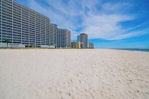 A beachfront hotel with multiple high-rise buildings, sandy beach, and a clear sky.