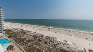 A beach with a pool, umbrellas, and beach chairs.