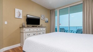 A hotel room with a large bed, a television on a dresser, and a balcony with a view.