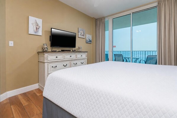 Habitación de hotel con una cama grande, un televisor en una cómoda y un balcón con vistas.