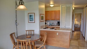 Un comedor con una mesa redonda de madera y sillas, una cocina con armarios de madera, y un pasillo que conduce a un dormitorio.