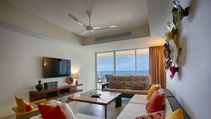 Una sala de estar con un sofá, sillones, una mesa de centro, un televisor de pantalla plana y un amplio ventanal con vista al mar.