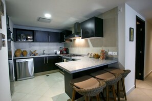 A modern kitchen with dark cabinets, a stainless steel dishwasher, a gas stove, and a bar area with stools.
