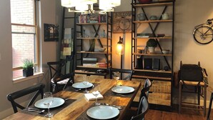 Een eetgedeelte met een houten tafel voor vier personen, omringd door stoelen. Er is een boekenkast met diverse spullen en een fiets hangt aan de muur.