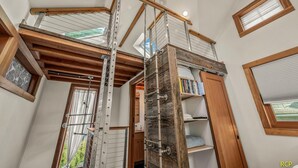 Een meerlaags interieur met een houten trap, metalen leuningen en een vide met boekenkasten.