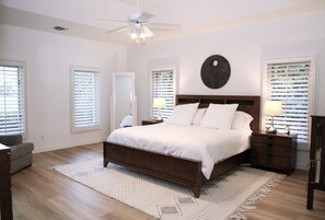 Un dormitorio con cama, ventilador de techo, mesita de noche, lámpara y reloj de pared.