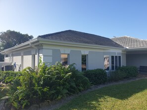 Una casa de una sola planta con techo gris, paredes exteriores blancas y un porche cubierto.