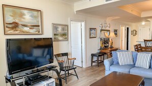 A living room with a flat-screen TV, a wooden coffee table, a blue sofa, and a dining area with a table and chairs.