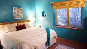 Un dormitorio con una cama grande, una ventana con persiana de madera, una lámpara de pared y un cuadro enmarcado.