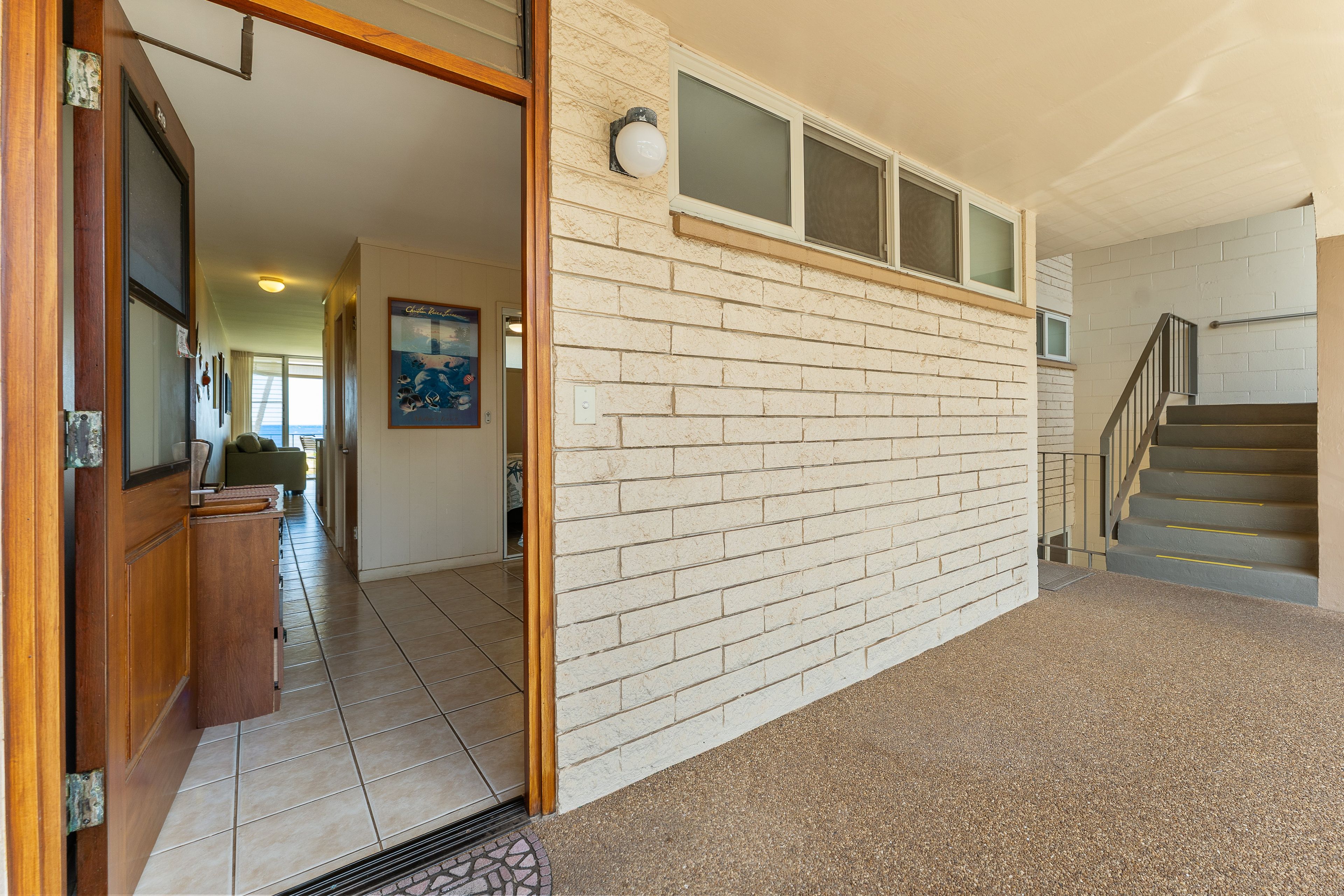 A hallway with a brick wall, a wooden door, and a staircase leading to an upper level.