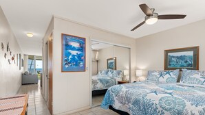Quarto de hotel com uma cama, ventoinha no teto, espelho grande e vista para o oceano.