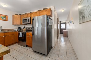 A modern kitchen with stainless steel appliances, wooden cabinets, and a tiled floor. - Second Floor Oceanview with Gorgeous Sunsets (Kihei)