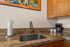 Una cocina con encimera de granito, pileta de acero inoxidable y cafetera.