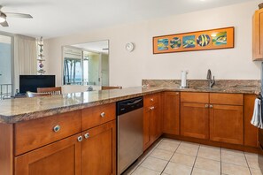 Una cocina con armarios de madera, lavavajillas, encimera de granito y un reloj en la pared.